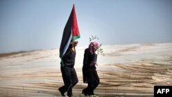 FILE - Man holding a Palestinian flag and a woman carrying an olive tree walk through rows of greenhouses on "Land Day," during which people plant olive trees near the Israeli border in Jabalia, northern Gaza, March 29, 2014.