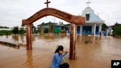A Cambodian woman pushes a church gate with an oar to steer her wooden boat in a flooded area along the Mekong river in Koh Phos village, Kandal province near Phnom Penh, Cambodia, Sunday, Sept. 29, 2013. (AP Photo/Heng Sinith)