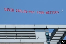 A message in support of the Hollywood writers' strike is pulled by an airplane in the sky above Boston University commencement ceremonies, Sunday, May 21, 2023, in Boston, during an address by David Zaslav, president and CEO of Warner Bros. Discovery. (AP Photo/Steven Senne)