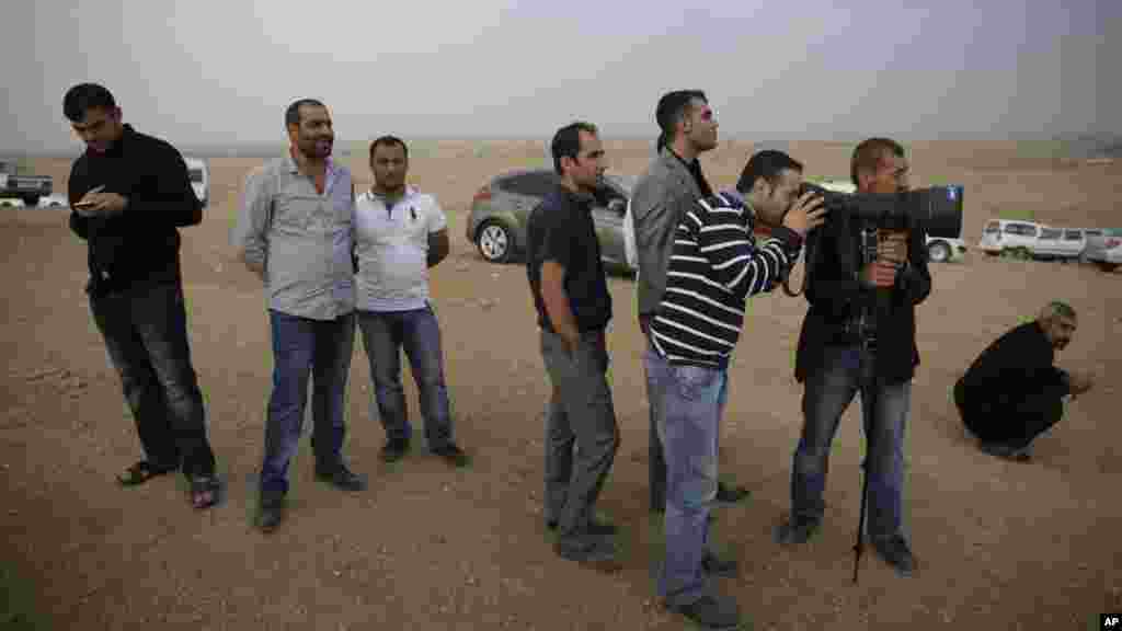Turkish Kurds wait to look through a press photographer's camera and telephoto lens to get a view of Kobani, Syria across the border, where Syrian Kurds and the militants of Islamic State group have been fighting, at a hilltop on the outskirts of Suruc, at the Turkey-Syria border, Sunday, Oct. 12, 2014.
