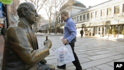 FILE - A shopper walks past a bronze sculpture of famed Boston Celtics coach Red Auerbach at Qunicy Market in downtown Boston.