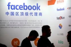 FILE - Visitors walk past the Facebook logo at the Global Mobile Internet Conference in Beijing, April 26, 2018.