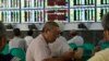 An investor uses his mobile phone in front of electronic screens showing stock information at a brokerage house in Wuhan, Hubei province, August 16, 2013. 