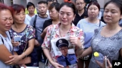 In this image taken from a video footage from AP Video, a woman holds up a photo of her son, a missing firefighter, outside a hotel where officials held a daily media conferences in northeastern China's Tianjin municipality, Aug. 16, 2015.