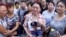 In this image taken from a video footage from AP Video, a woman holds up a photo of her son, a missing firefighter, outside a hotel where officials held a daily media conferences in northeastern China's Tianjin municipality, Aug. 16, 2015.