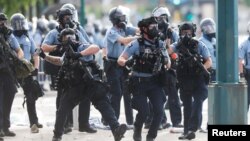 Seorang petugas kepolisian melempar tabung-tabung asap untuk membubarkan massa yang berdemo dekat kantor polisi Minneapolis, AS, 27 Mei 2020, setelah kematian seorang Afrika-Amerika, George Floyd, saat diamankan polisi. (Foto: Reuters) 