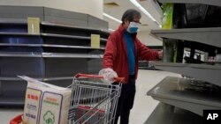 Seorang pria yang mengenakan masker dan tas plastik sebagai sarung tangan berjalan melewati rak kosong kertas tisu di sebuah supermarket di Hong Kong, Jumat, 7 Februari 2020. (Foto: AP)