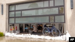 Fitness trainer Kelly Curtis, right, works out at her studio protected with sandbags in preparation for a storm along the Peninsula in Long Beach, Calif., Feb. 19, 2024.