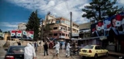 FILE - In this March 24, 2020 file photo, workers spray disinfectant to prevent the spread of the coronavirus, on a street lined with billboards showing Syrian President Bashar Assad, in Qamishli, Syria.
