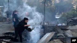 Residents spray water over remains of their homes after a wildfire damaged dozens of houses on the outskirts of Valparaiso, Chile, Dec. 25, 2019. 