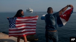 Yaney Cajigal, left, and Dalwin Valdes hold up U.S. and Cuban flags as they watch the arrival of Carnival's Adonia cruise ship from Miami, in Havana, Cuba, May 2, 2016.