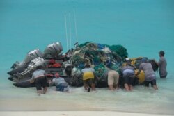 FILE - In this April 10, 2021, photo provided by Matthew Chauvin, workers with the Papahanaumokuakea Marine Debris Project push boats loaded with fishing nets and plastic off Kure Atoll in Hawaii.