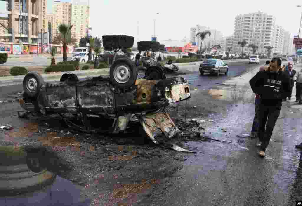 People walk past a burned car following clashes between supporters of Egypt's ousted President Mohamed Morsi and riot police in Cairo's Nasr City, Jan. 8, 2014.