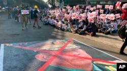 FILE - A large image that has an X mark on the face of Commander in chief Senior Gen. Min Aung Hlaing, also chairman of the State Administrative Council, lies on a road as anti-coup protesters gather outside the Hledan Centre in Yangon, Myanmar, Feb. 14, 2021.
