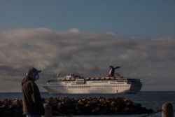 A man wearing a face mask as a preventive measure against the spread of the COVID-19 Coronavirus, looks at Cruise Ships docked at the port due to a no-sail order in Long Beach, California on April 11, 2020.