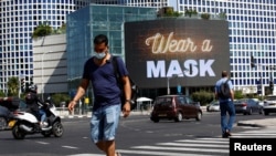People walk near a billboard as Israel imposes a second nationwide coronavirus disease (COVID-19) lockdown amid a rise in infections ahead of Yom Kippur in Tel Aviv, Israel, Sept. 27, 2020. 