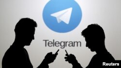 Two men pose with smartphones in front of a screen showing the Telegram logo in this picture illustration taken in Zenica, Bosnia and Herzegovina November 18, 2015. (REUTERS/Dado Ruvic)