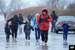 Para imigran berlari di tengah hujan menuju tenda-tenda di lokasi perumahan migran di Floyd Bennett Field, kawasan Brooklyn, New York, 9 Januari 2024. (Mary Altaffer/AP)