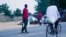 A cyclist rides past Civilian Joint Force members who are patrolling the streets looking for Boko Haram fighters. Maiduguri, Nigeria. (C. Oduah for VOA)