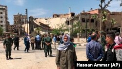 SYRIA -- Policemen and civilians stand in front of damaged buildings in the town of Douma, the site of a suspected chemical weapons attack, near Damascus, April 16, 2018