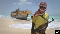 FILE - A masked Somali pirate stands near a Taiwanese fishing vessel that washed up on shore after the pirates were paid a ransom and released the crew, Sept. 23, 2012.