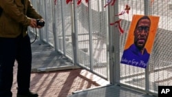 A passerby stops to take a photo of a George Floyd picture hanging on the fence surrounding the Hennepin County Government Center in Minneapolis where the trial of former Minneapolis police Officer Derek Chauvin continues, April 2, 2021.