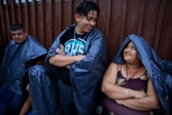 Migrants from El Salvador talk as they wait in the rain outside the Mexican Commission for Refugee Assistance office where hundreds a day line up to seek a document permitting them to legally be in the country in Tapachula, Mexico, June 13, 2019.