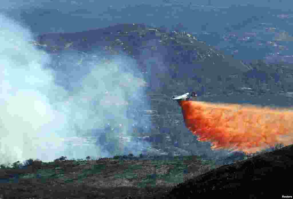 Sebuah pesawat menjatuhkan air di lokasi kebakaran hutan di kawasan perbukitan dekat San Marcos, California.