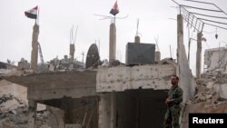 A Syrian army soldier stands at a damaged site in al-Hajar al-Aswad neigborhood, which was recaptured from Islamic State group militants on Monday. May 22, 2018.