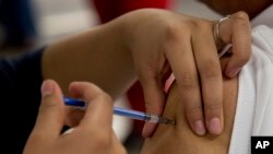 FILE - A woman gets a vaccination from a nurse in Mexico City, Jan. 27, 2014.