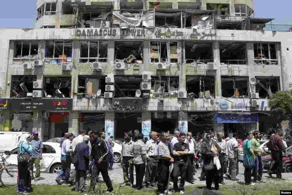 People stand on a street lined with a damaged building and destroyed cars after a blast at Marjeh Square in Damascus, April 30, 2013. 