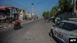 FILE - People ride a motorcycle past a police car following a call for a general strike launched by several professional associations and companies to denounce insecurity in Port-au-Prince on Oct. 18, 2021.