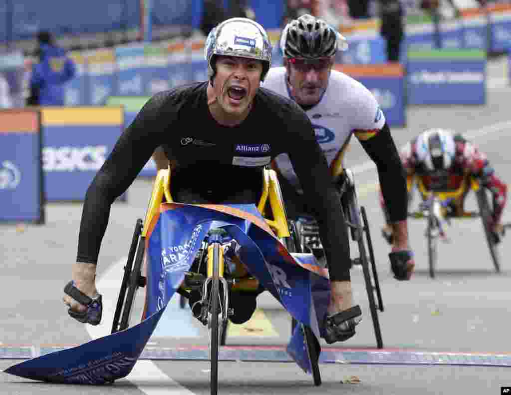 Marcel Hug dari Swiss melewati garis finish diikuti oleh Ernst Van Dyk dari Afrika Selatan dan Kurt Fearnley dari Australia saat memenangkan kategori kursi roda pria.
