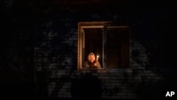 Catherine, 70, looks out the window while holding a candle for light inside her house during a power outage, in Borodyanka, Kyiv region, Ukraine, Thursday, Oct. 20, 2022. 