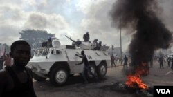 Kendaraan pasukan keamanan PBB melewati para suporter Alassane Ouattara yang berdemo di Abidjan.