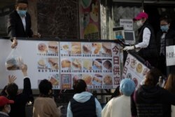 A worker hands down a bag of bread outside a bakery in Beijing, March 23, 2020. While social distancing remains the norm, China is striving to restore activity in the world's second-largest economy after the shutdown over the coronavirus outbreak.