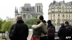 FILE - People hug while looking at Notre-Dame-de-Paris in the aftermath of a fire that devastated the cathedral, April 16, 2019. 