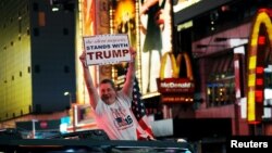 Un homme jonché sur son véhiculé brandit une pancarte qui dit que la grande majorité silencieuse soutient Donald Trump à Times Square, New York, 9 novembre 2016.