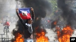 Seorang demonstran mengibarkan bendera Haiti saat protes menuntut pengunduran diri PM Ariel Henry di Port-au-Prince, Haiti, Jumat, 1 Maret 2024. Dewan penguasa transisi Haiti dijadwalkan akan dilantik padaKamis (25/4). (Foto: AP)