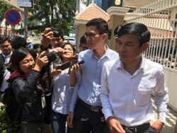 Journalist Yeang Sothearin, second from right, speaks to reporters as he and co-accused Uon Chhin leave municipal court in Phnom Penh, Cambodia, July 26, 2019.