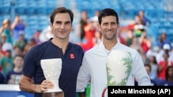 Novak Djokovic (kanan) memegang trofi turnamen tenis Rookwood Cup setelah mengalahkan Roger Federer (kiri), di Mason, Ohio, 19 Agustus 2018.