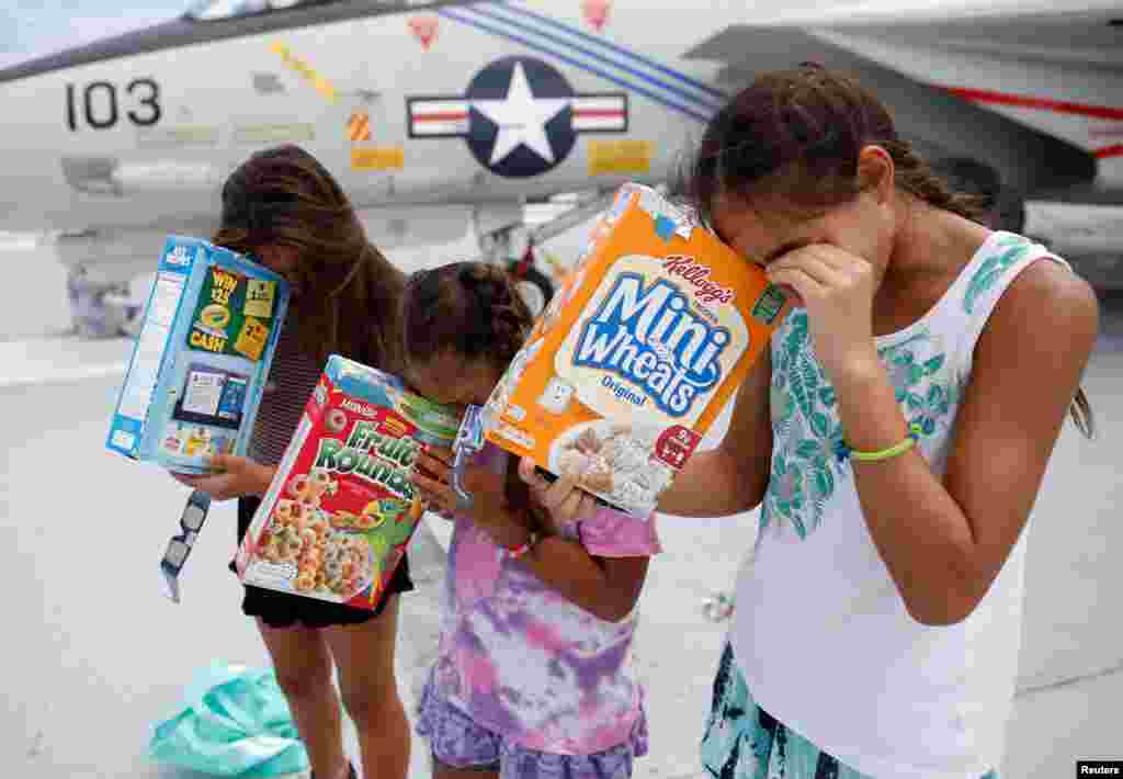 Michelle Campano (Right) and her sisters Jennifer (Middle) and Lauren Campano, all of Rockville, Maryland, check on the position of the sun using homemade solar viewers from the flight deck of the Naval museum ship U.S.S. Yorktown during the Great America