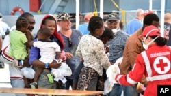 FILE - Migrants line up at a Red Cross tent after they disembarked from the Irish Navy vessel LE Niamh at the Messina harbor in Sicily, Italy, Aug. 24, 2015.