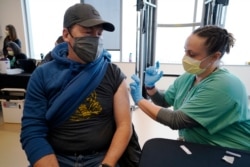 FILE - Brian Kennedy, a teacher at Green Valley Elementary School, receives a COVID-19 vaccination from nurse Arielle Goode during a mass vaccination of Denver Public Schools employees at Denver Health, Feb.13, 2021.