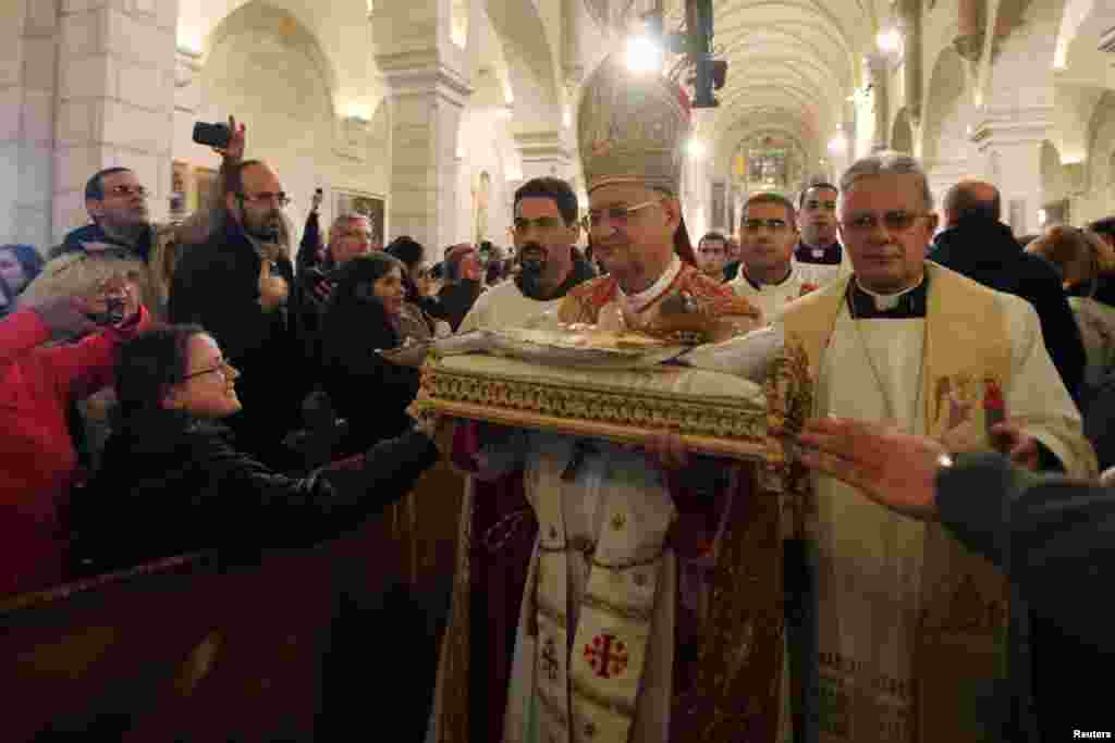 Uskup Yerusalem Fouad Twal membawa patung bayi Yesus pada perayaan Misa Natal di gereja St. Catherine, yang terhubungkan dengan gereja Nativitas, tempat kelahiran Yesus di Bethlehem, Palestina.&nbsp; 