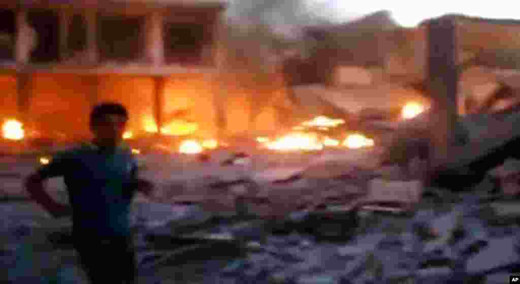 This image taken from video obtained from the Shaam News Network shows a Syrian man walking near destruction and fire caused by a bomb that hit Binnish town, Idlib province, Sept. 5, 2013. 