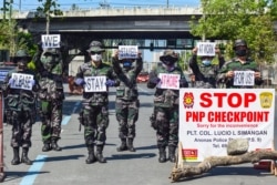 Police personnel hold up placards reminding people to stay at home amid concerns of the spread of the COVID-19 coronavirus in Manila on March 31, 2020.