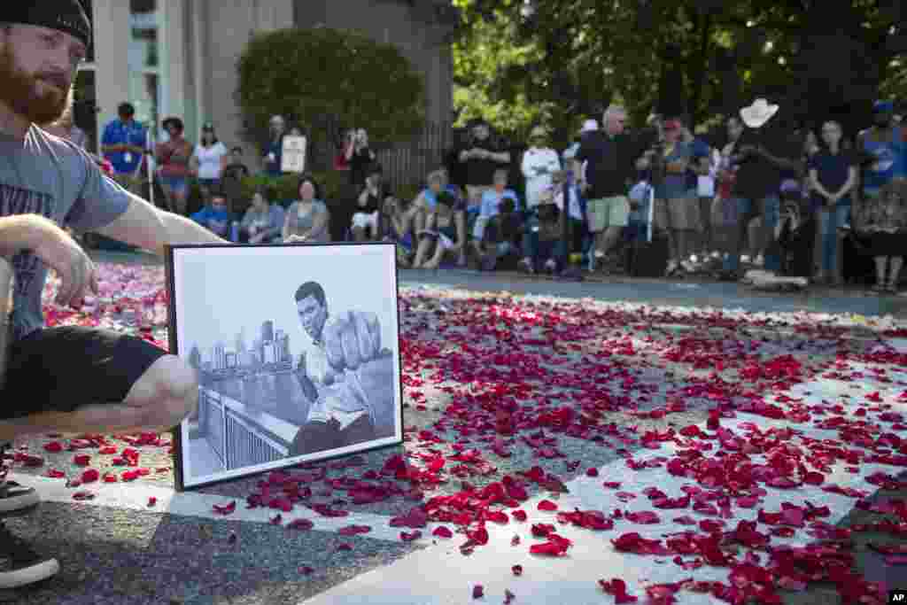 Nick Smith, of Louisville, poses for a photograph holding a drawing of Muhammad Ali as spectators wait for the arrival of Ali's funeral procession to enter Cave Hill Cemetery, Friday, June 10, 2016, in Louisville, Kentucky. 