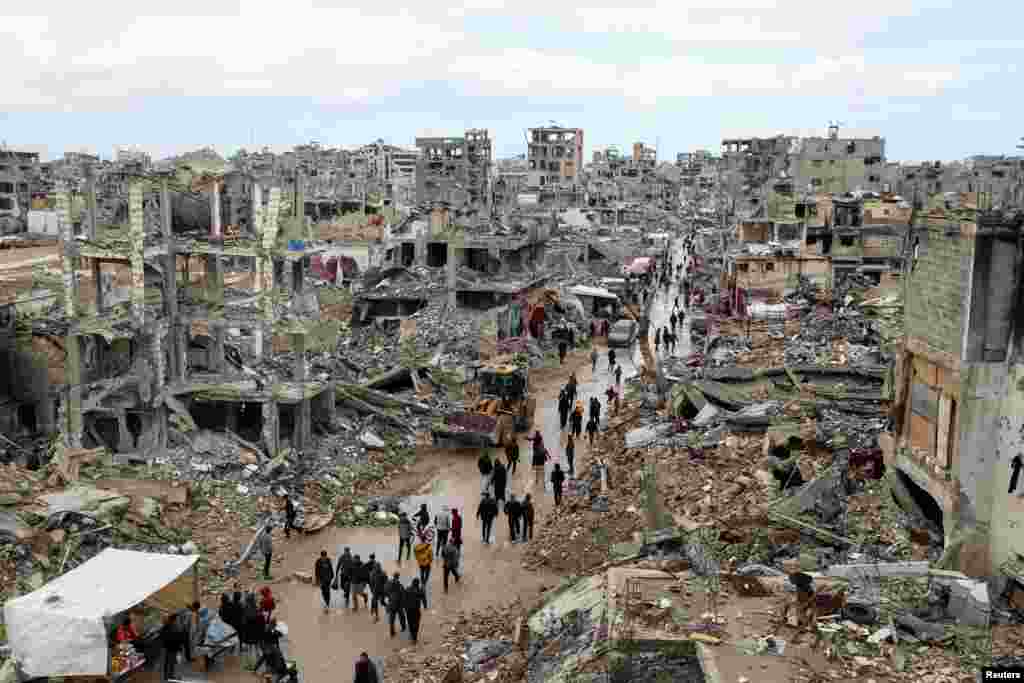 Palestinians walk past the rubble of buildings destroyed during the Israeli offensive, on a rainy day in Gaza City amid a ceasefire between Israel and Hamas.