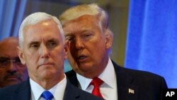 Le président élu des Etats-Unis Donald Trump, arrière-plan, soufle quelques choses à l’orielle de son vice-président Mike Pence lors d’une conference de presse à la tour Trump, à New York, 11 janvier 2017.